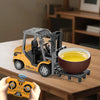 A yellow 1:64 scale remote control excavator is shown lifting a bowl of yellow liquid on a wooden table.