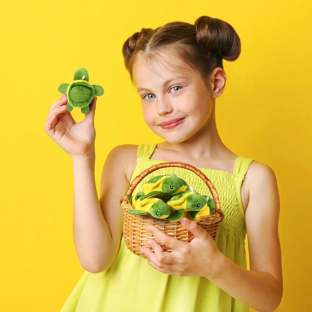 A young girl holds a green sea turtle plush toy in her hand against a yellow background.