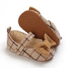 A pair of tan soft cotton baby walking shoes with anti-slip soles and a bow detail.