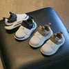A pair of white and black kids' everyday sneakers with easy velcro straps resting on a dark surface.