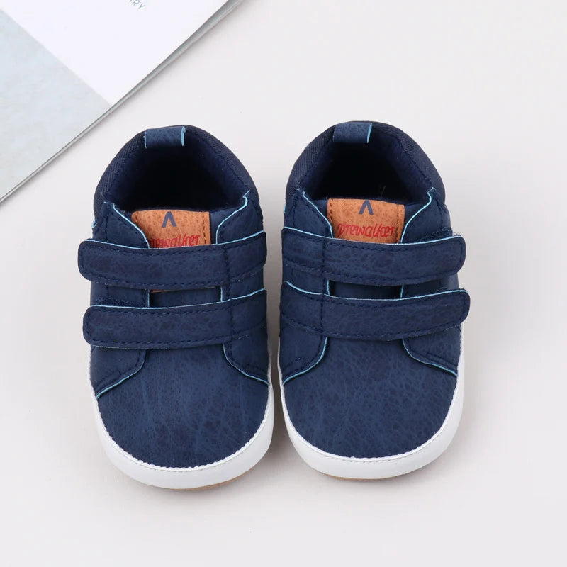 A pair of navy blue baby first walker shoes with brown accents and white soles.