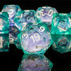 A close-up of a set of iridescent teal and purple liquid core dice used for tabletop gaming.