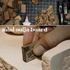 A close-up of a mini Ouija board being held by a hand, showing the wooden letters and markings.
