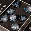 A silver tray holds a set of handmade liquid core polyhedral dice with a galaxy finish scattered on a dark surface.