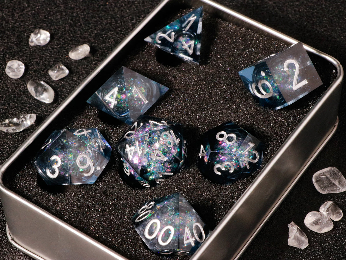 A silver tray holds a set of handmade liquid core polyhedral dice with a galaxy finish scattered on a dark surface.