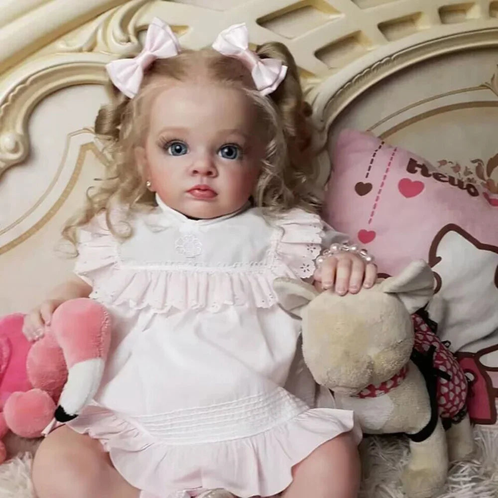 A lifelike reborn baby doll with pink dress and accessories sitting in a light-colored setting.