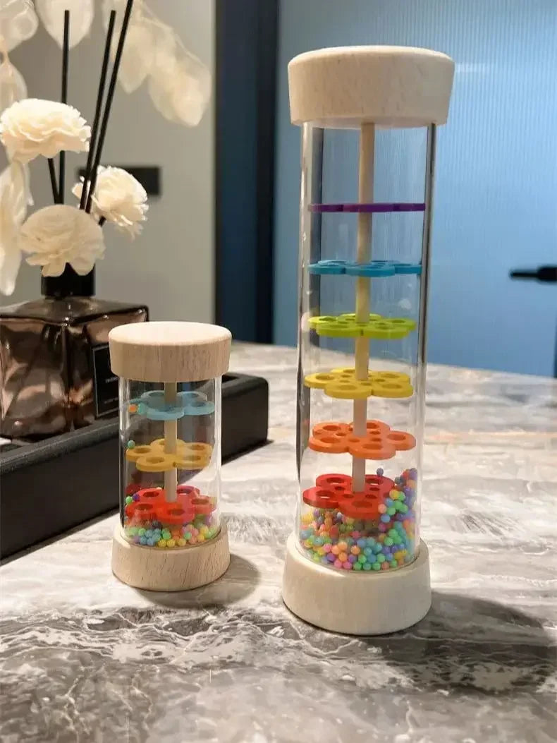 A clear wooden rain sound shaker toy with colorful plastic elements stacked inside a tall wooden holder.