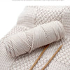 A skein of light beige cotton yarn is shown rolled on a knitted fabric with knitting needles.