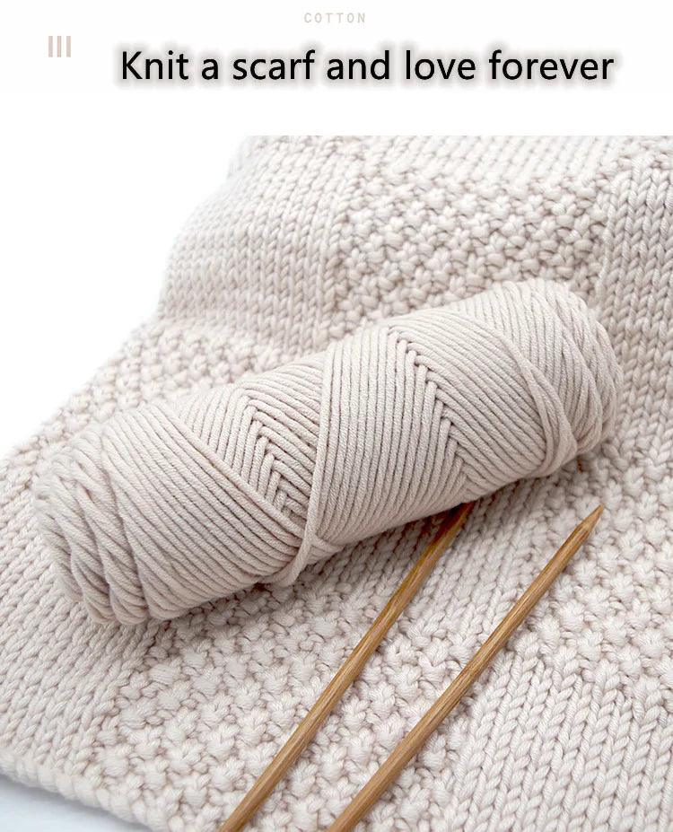 A skein of light beige cotton yarn is shown rolled on a knitted fabric with knitting needles.