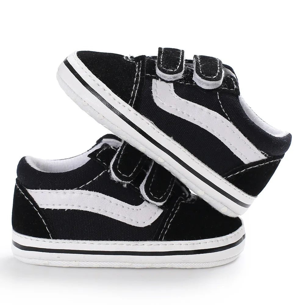 A pair of black and white striped canvas baby sneakers shown from the side.