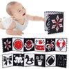 A baby smiles while holding a black and white sensory cloth book with various patterns.