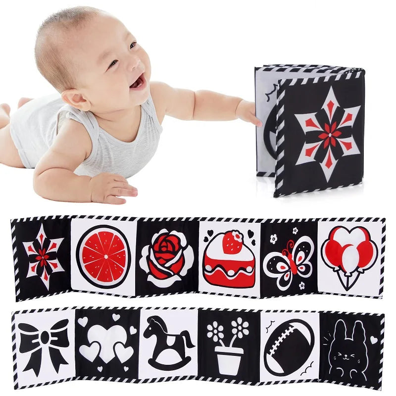 A baby smiles while holding a black and white sensory cloth book with various patterns.