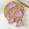 A pink knitted doll outfit set for a baby doll featuring a hat, top, and leg warmers, displayed on a woven mat.