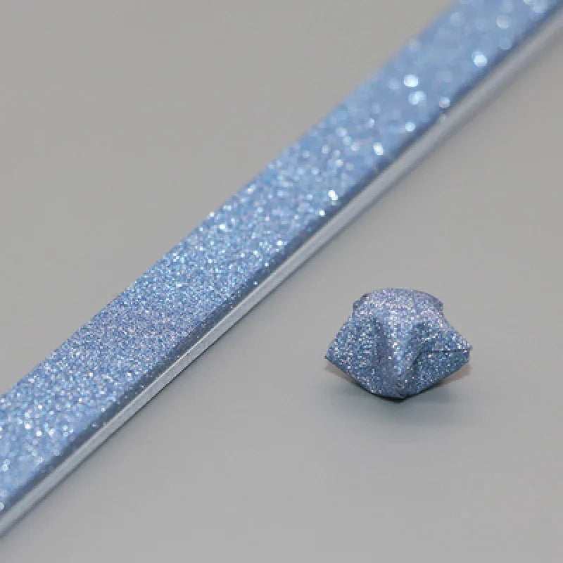 A close-up view of a light blue glitter paper strip and a small piece of folded origami star paper.