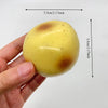 A hand holds a yellow, spherical potato stress ball with brown spots against a white background.