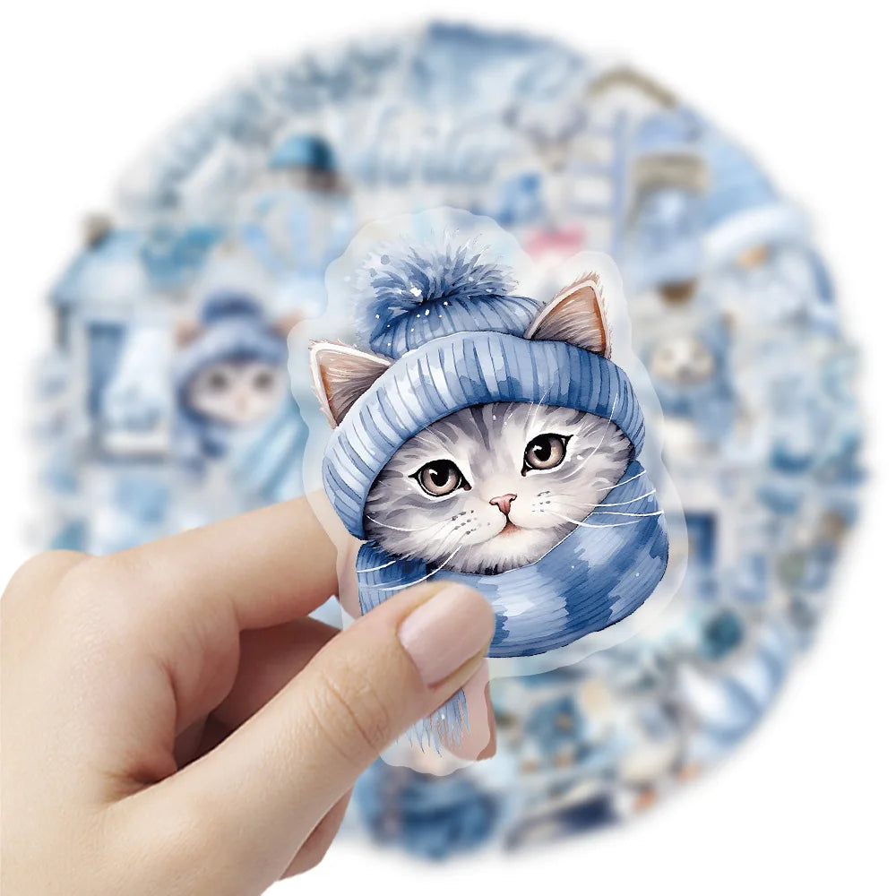 A hand holds a blue knitted cat sticker featuring white fur and large ears against a light blue watercolor background.