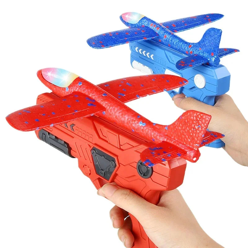Une main tient un lanceur d'avion en mousse orange avec des ailes rouges et des accents bleus, à côté d'un planeur bleu.