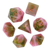 A set of pink and green glitter resin polyhedral dice, including a d20 and other shapes.