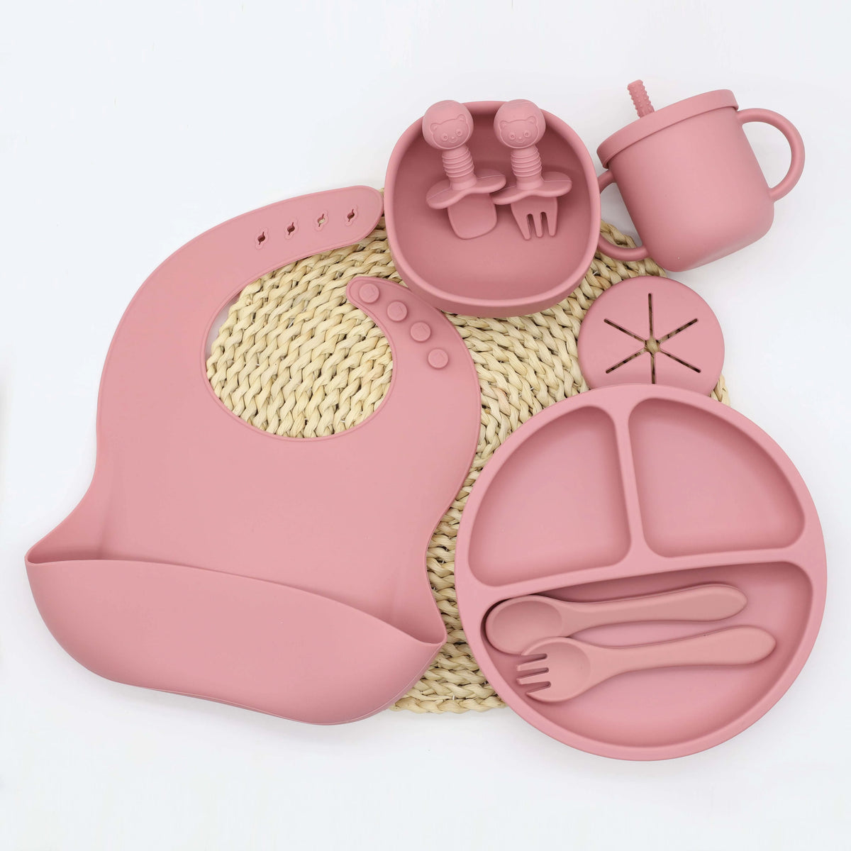 A pink silicone tableware set for babies including a cup, spoon, fork, and plate with suction cups.