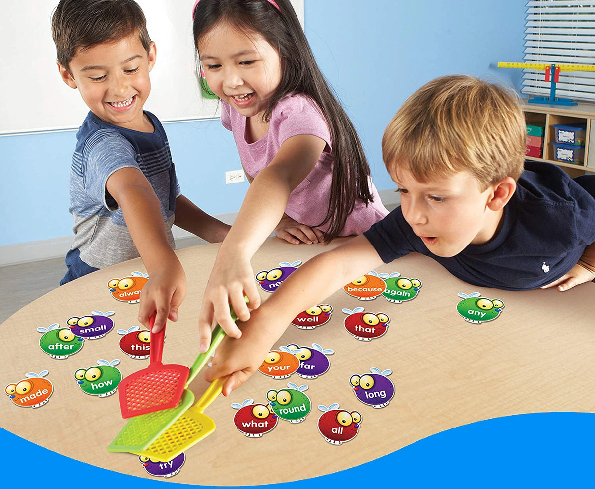 Three children are playing with a colorful fly swatter game set on a wooden table.