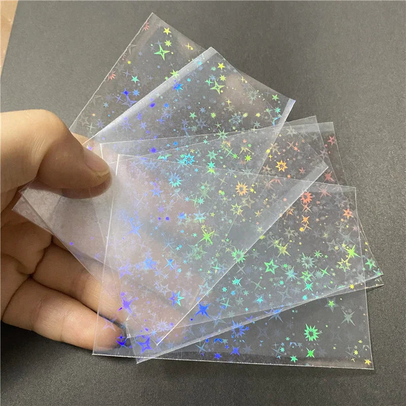 A hand holds a stack of holographic card sleeves featuring colorful star and glitter designs.