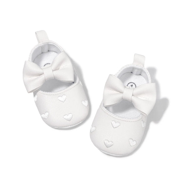 A pair of white baby shoes with a bow detail for first walkers.