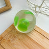 A translucent green squishy stress ball shaped like a kiwi fruit resting on a wooden cutting board.