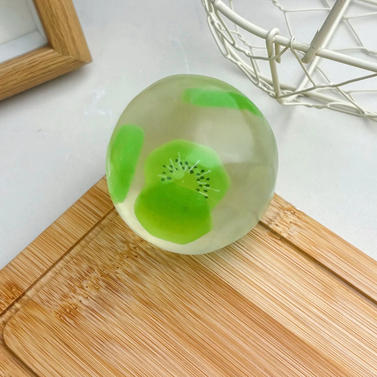 A translucent green squishy stress ball shaped like a kiwi fruit resting on a wooden cutting board.