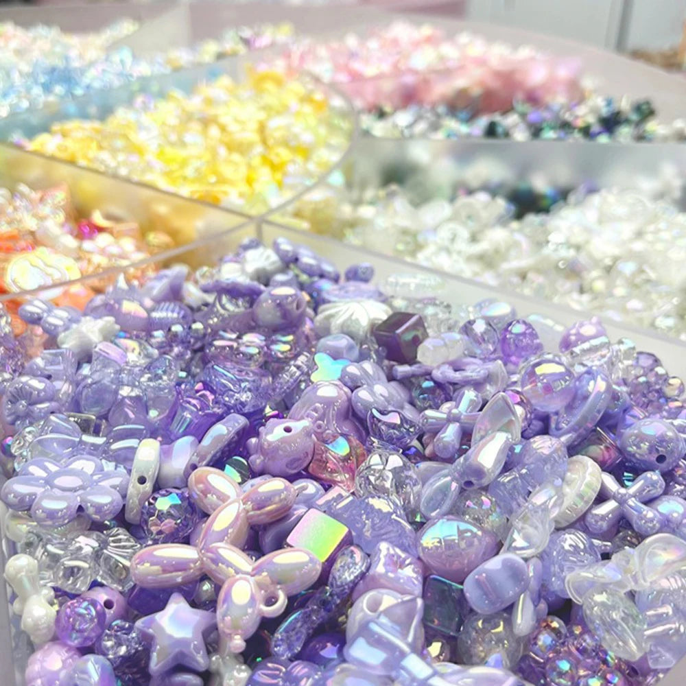 A close-up of purple and iridescent acrylic bow and flower beads used for DIY jewelry making.