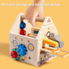 A wooden busy house toolbox with various gears, levers, and a screwdriver component is shown being held by a hand.