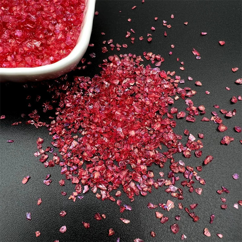 Crushed red glass crystals scattered on a dark surface with a white bowl partially visible.