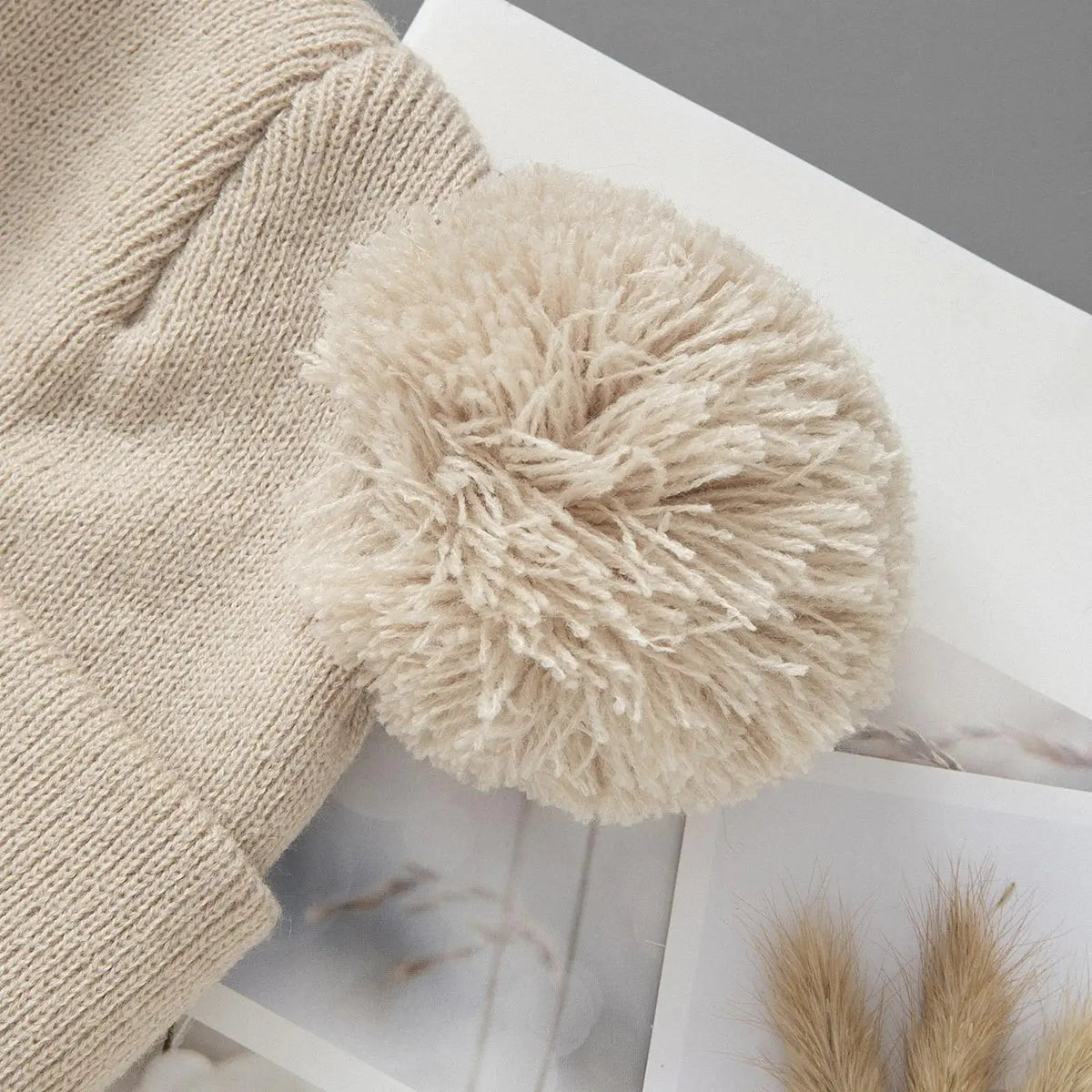 A fluffy beige knit baby beanie hat resting on a white surface.