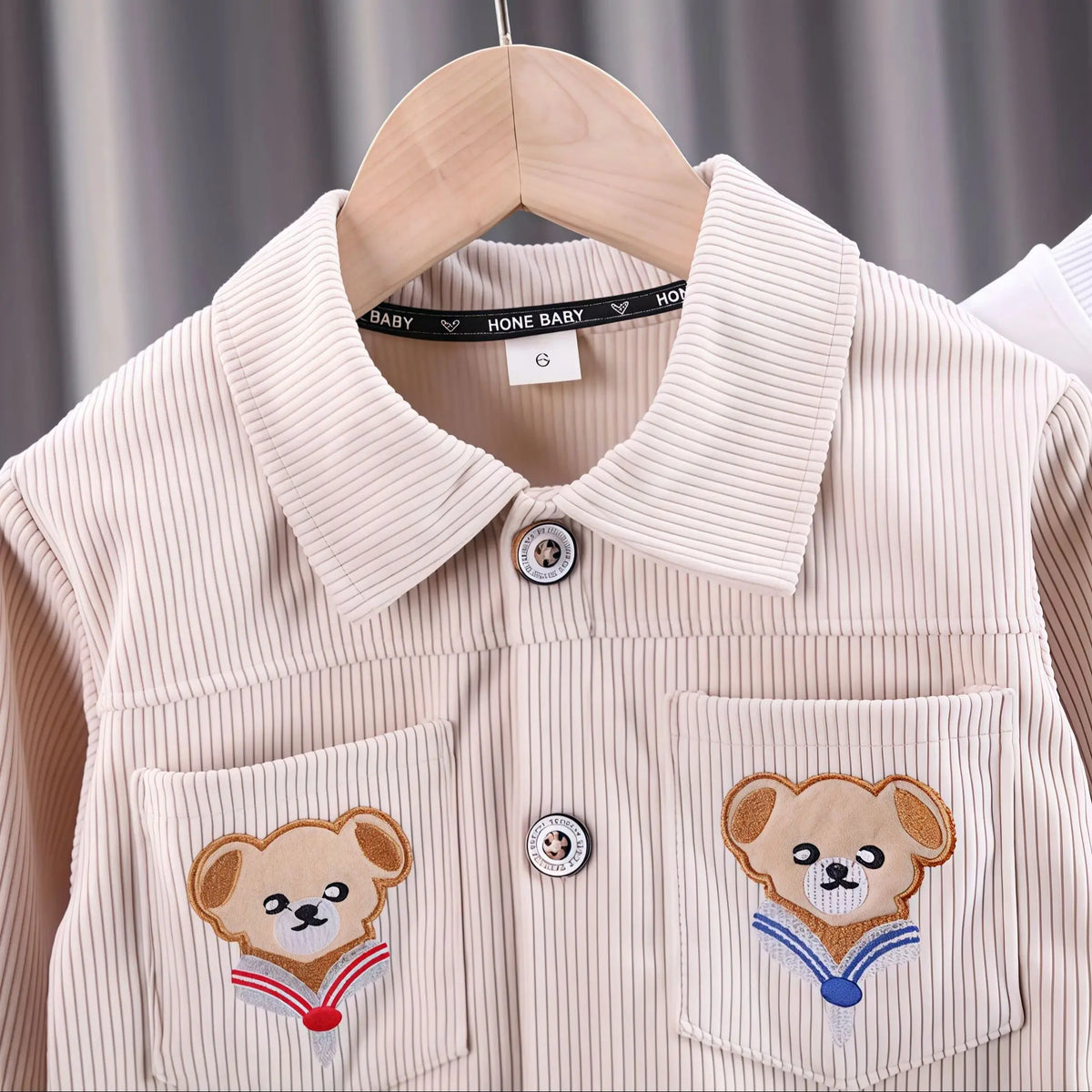 A light beige corduroy jacket with embroidered bear patches on the chest pockets.