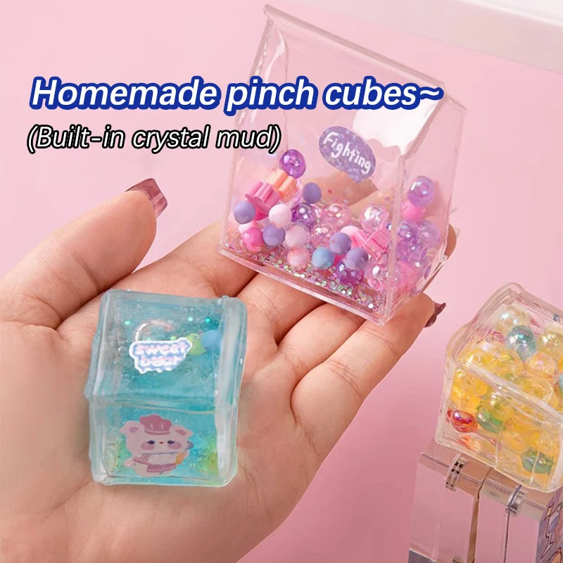 A hand holds a clear plastic pinch cube filled with colorful beads and another finished cube.