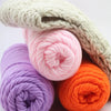 A close-up of various skeins of soft, pastel colored milk cotton yarn in purple, pink, and orange.