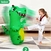 A green inflatable dinosaur punching bag is shown next to a young girl in a white gi, indoors.