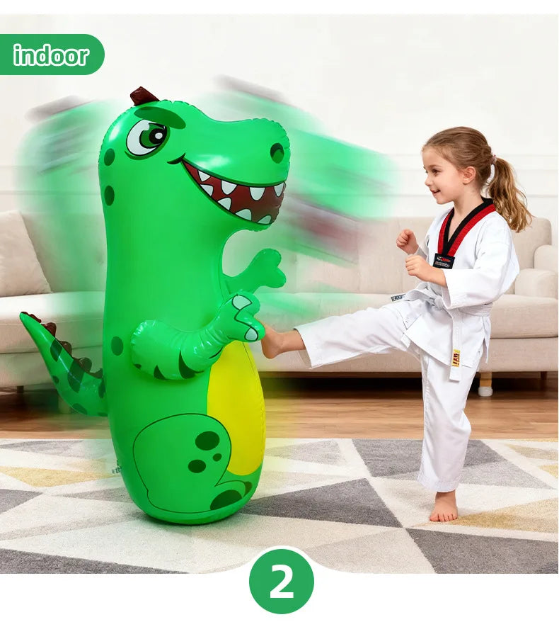 A green inflatable dinosaur punching bag is shown next to a young girl in a white gi, indoors.
