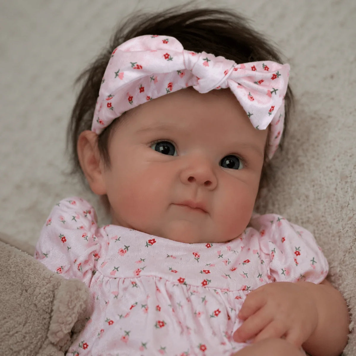 A close-up photo of a baby doll with hand-rooted hair wearing a pink floral outfit and a matching bow.