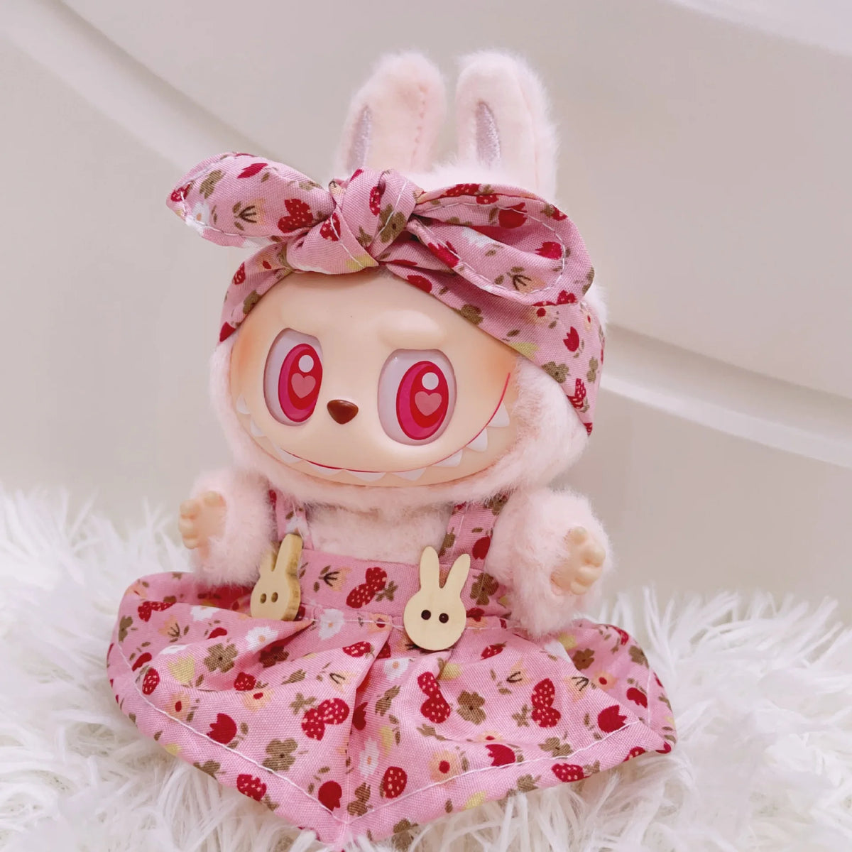 A fluffy pink bunny doll wearing a floral dress and bow, with strawberry themed accessories.