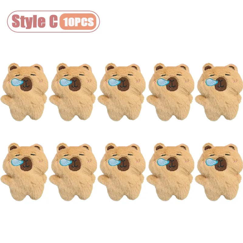 Ten small, light brown plush toys shaped like capybaras with blue tongues.