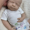 A lifelike 18-inch silicone reborn baby doll named Pascale wearing a white shirt and diaper, photographed from above.
