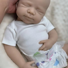 A lifelike 18-inch silicone reborn baby doll named Pascale wearing a white shirt and diaper, photographed from above.