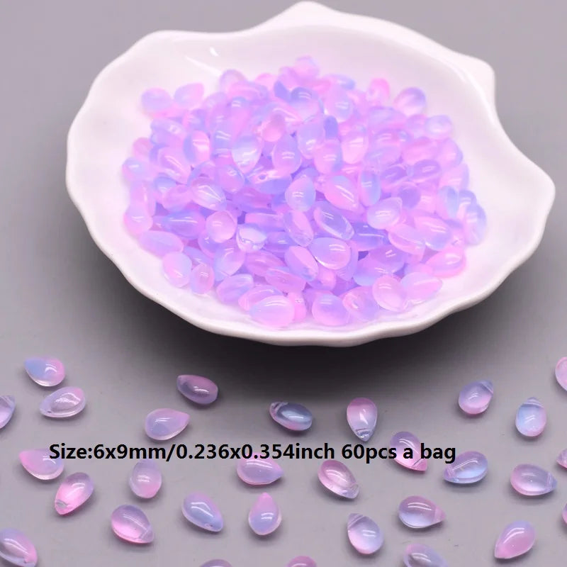 A pile of translucent purple and pink water drop glass beads in a white dish.