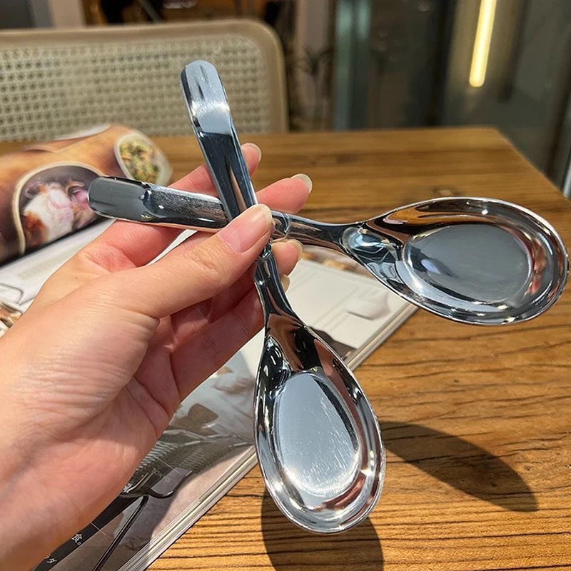 A hand holds a silver spoon and fork on a wooden table.