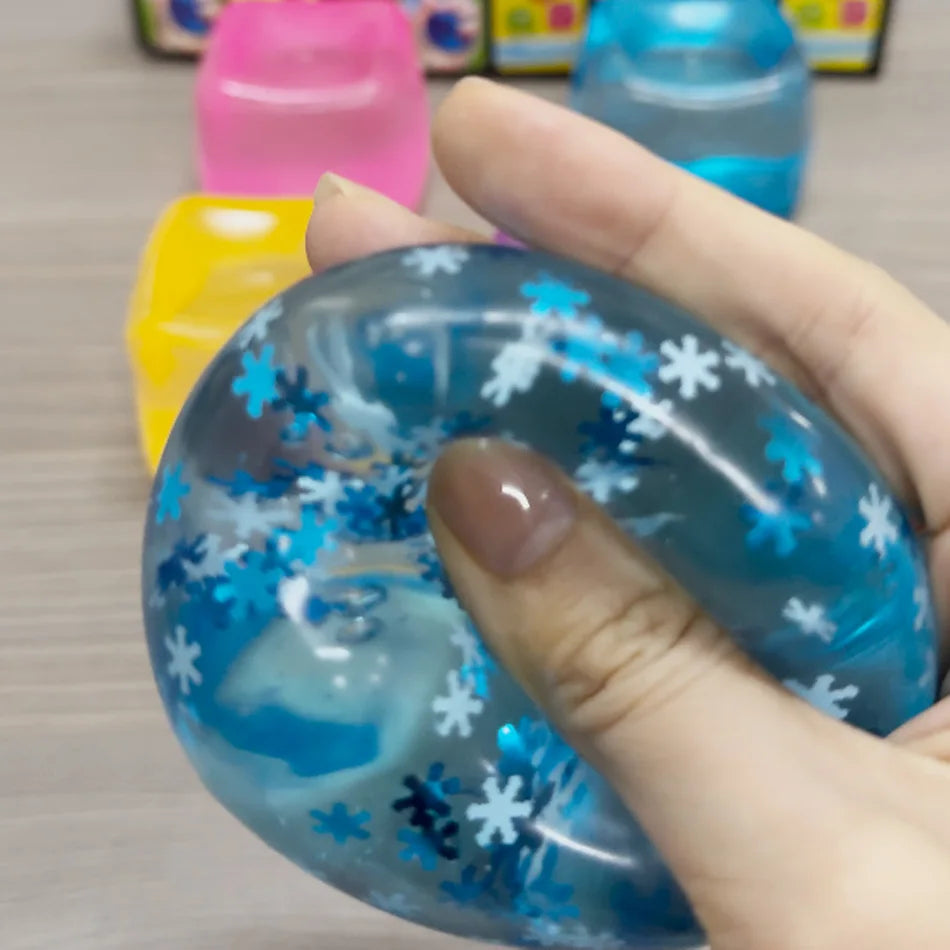 Une main tient un jouet squishy bleu translucide en forme d'anneau avec des motifs de flocons de neige blancs.
