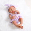 A lifelike vinyl reborn doll with a purple outfit and a matching bow on her head.