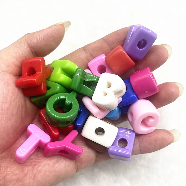 A hand holds ten mixed colored alphabet letter beads for DIY jewelry making