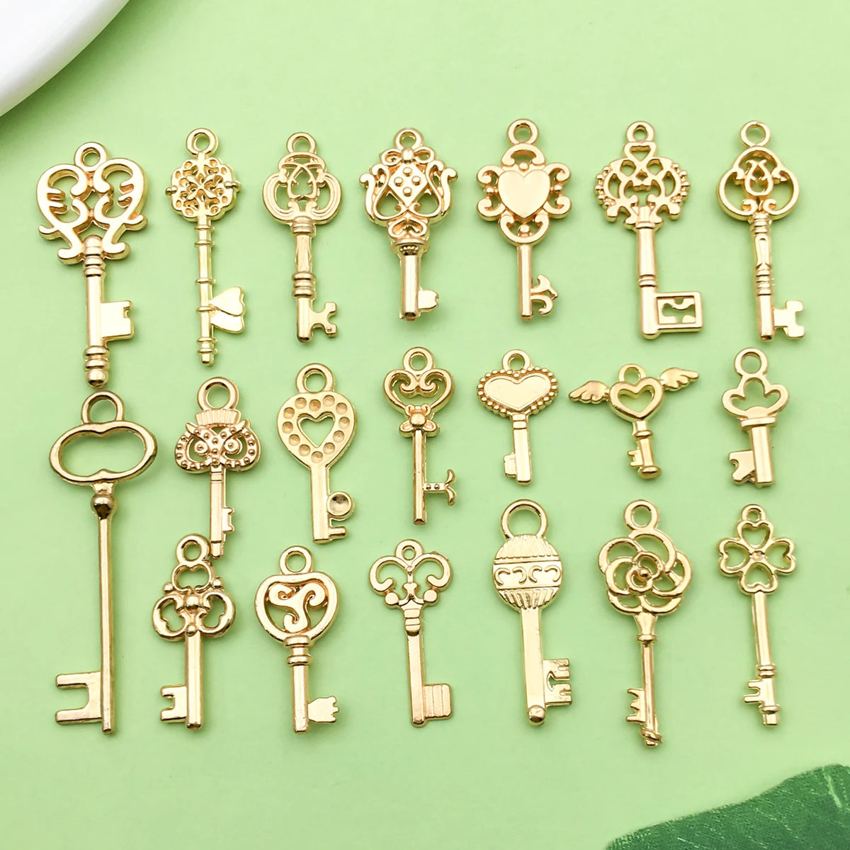 A collection of vintage gold-toned key charms and pendants for jewelry making displayed on a light green surface.