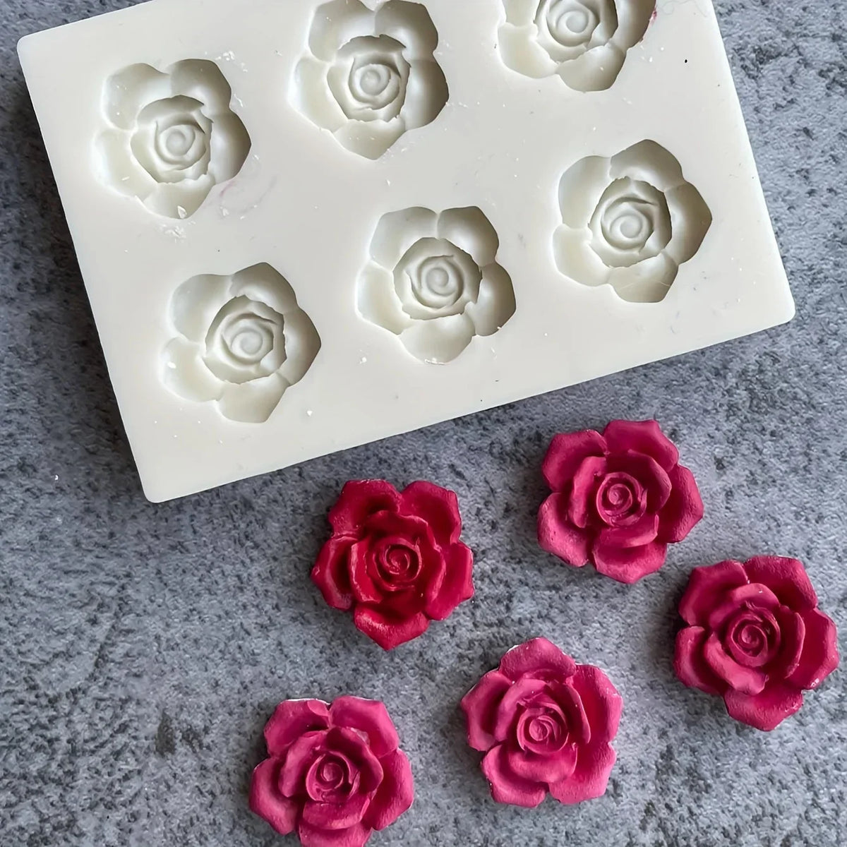 A silicone mold with multiple rose flower shapes for candle and soap making is shown on a gray surface.