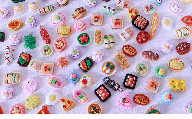 A collection of colorful miniature dollhouse snack foods including candies, jellies, and pastries arranged on a white surface